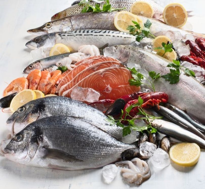 Pesce, crostacei e molluschi disposti su ghiaccio con limone e prezzemolo